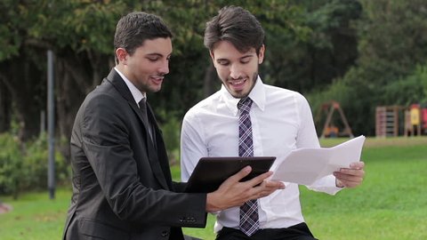 Two business people with tablet computer talk about a project on a park
