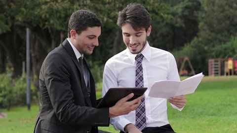 Two happy business people with tablet computer talk about a project on a park