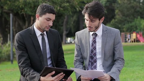 Two business people with tablet computer talk about a project on a park bench
