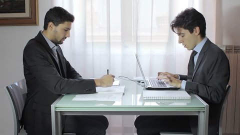 Two businessmen using digital tablet and laptop at desk in office