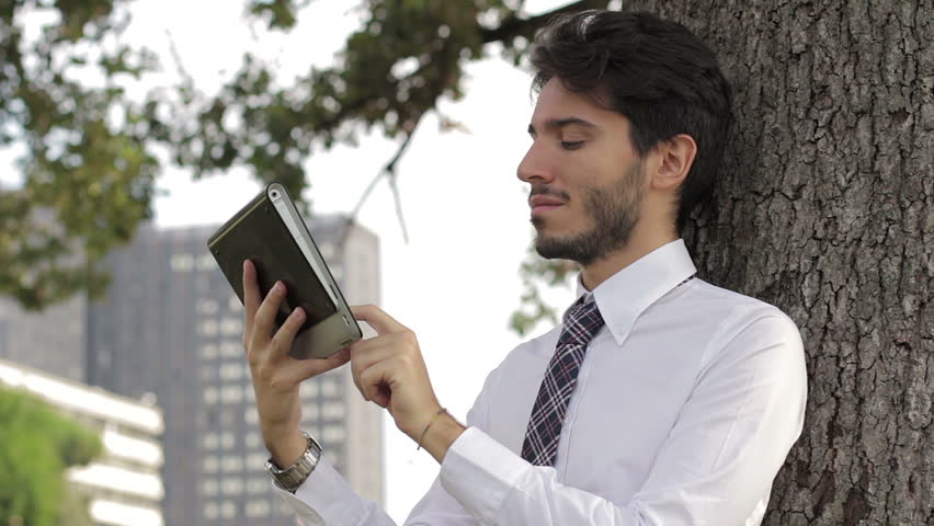 Young businessman beneath the tree using tablet