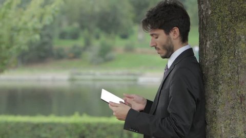 Young businessman beneath the tree using tablet