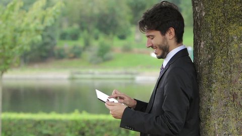 Happy business young man using tablet PC outside on a park