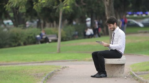 Happy business man using tablet PC outside on a park