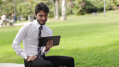Happy business young man using tablet PC outside on a park