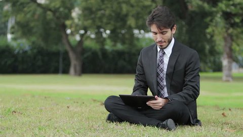 Happy business man using tablet PC outside on a park