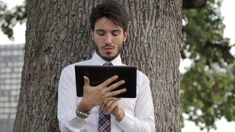 Young businessman beneath the tree using tablet