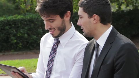 Two businessmen looking at the tablet computer on a park bench