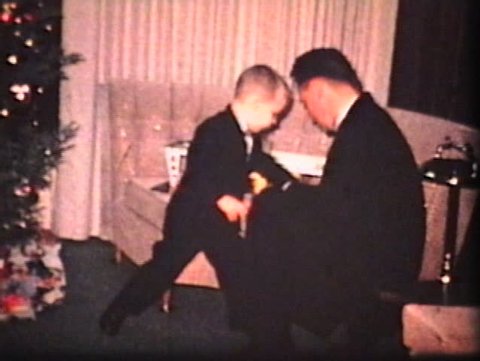 A young father spends time with his son looking at presents and hanging out by the Christmas tree. (Vintage 8mm film)