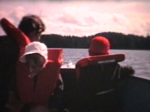 A mother and her two children enjoy a nice boat ride on the lake while their father drives the boat. (Vintage 8mm film)