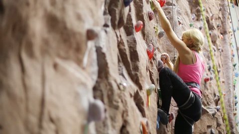 Pretty blonde woman with special equipment climbs on wall