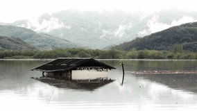 Cinematic look.Flooded wooden building in the muddy lake water after big storm and heavy downpour, rain falling,clouds on the hills.Submerged ruin after hurricane.Similar clip available 24 or 30 fps. 
