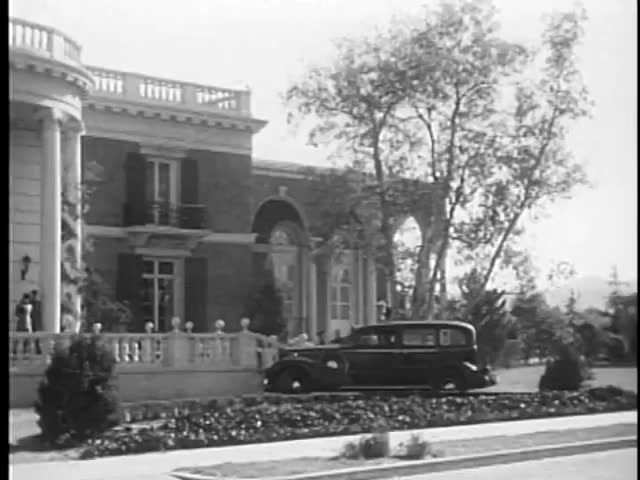 Car rushing past people in front of building entrance, 1930s