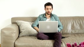 Young adult man sitting on couch in living room and having video chat