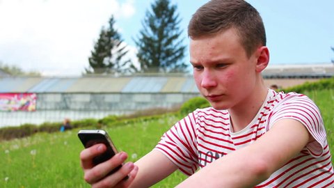 boy presses the sensor number, sitting on green grass in the park
