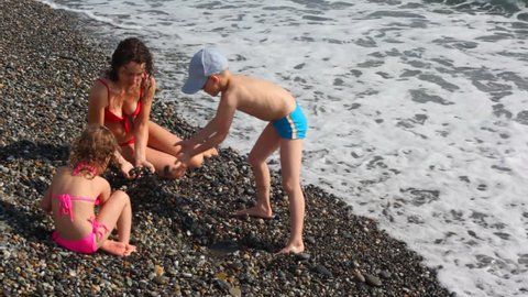 mother with childes doing pile up of pebbles in surf sea beach 