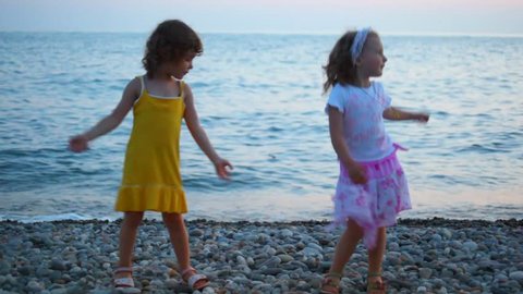 two little girls dancing in evening pebble beach, sea in background 