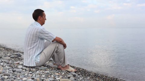 man sitting on pebble coast and looks on sea 