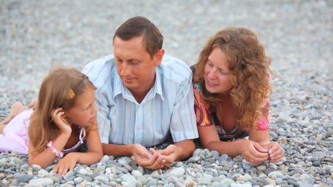 happy family lying on pebble beach and talking 
