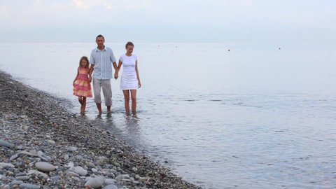 family walking in sea surf, join hands, to camera 