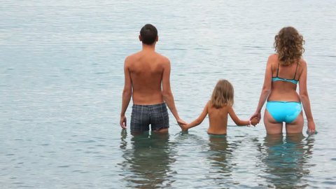 family of three persons standing in sea, join hands 