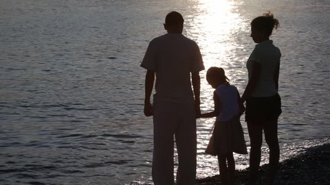 silhouettes of family standing in beach and looking to sea 