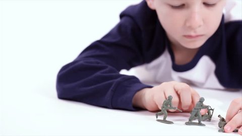 A young boy plays with old fashion toy soldiers. Taken on a white backdrop. Dolly shot.