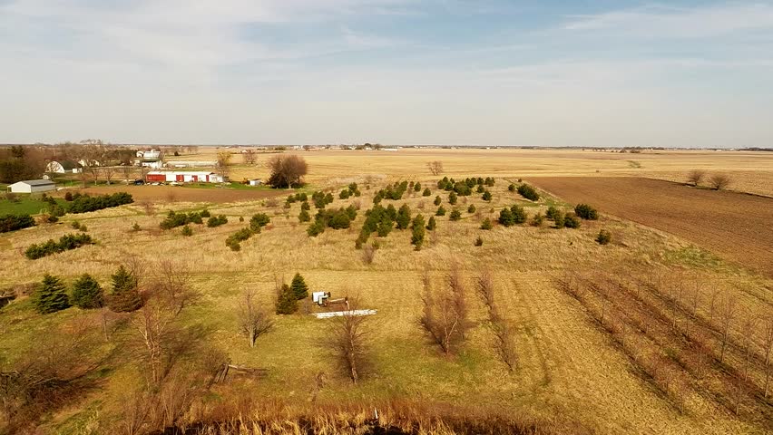 Aerial view flyover Illinois farmland in early spring with creek open fields and country house