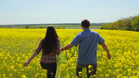 Man and woman in a shirt with long hair and goes on spring flowering rapeseed field in Ukraine