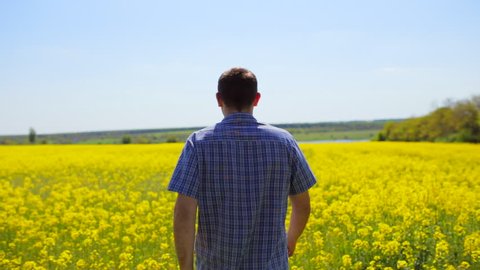 The guy in the jacket goes on spring flowering rapeseed field in Ukraine