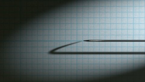 A closeup view closeup pan of a polygraph lie detector test needle drawing a red line on graph paper