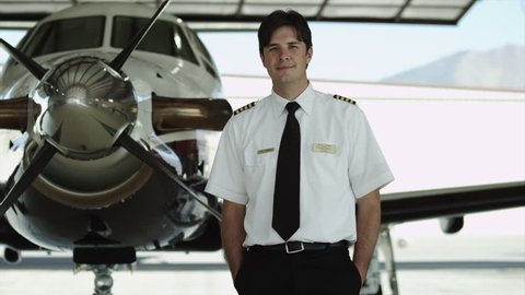 Medium Shot Pan Portrait of pilot in hangar with private airplane in background
