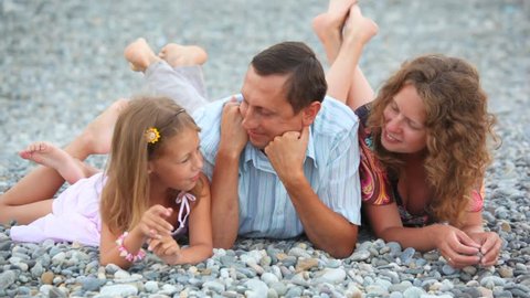 smiling family lying on pebble beach and talking 