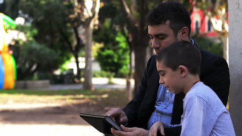 Father and Son Having Fun Using Touch Pad Computer Tablet Outside.