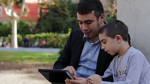 Son and father using tablet together in park