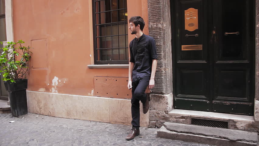 One twenties young man leaning on a wall outdoors in grungy setting