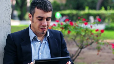 Man at a park using a computer tablet computer looking at camera