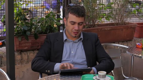 Businessman working on tablet computer and drinking coffee in cafe