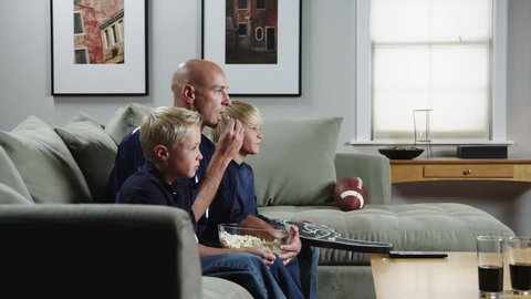 Medium Shot Father with two sons (8-9, 10-11) watching match in TV and eating popcorn 