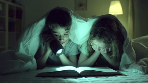 Children reading one book, girl blocking vision to boy with her finger