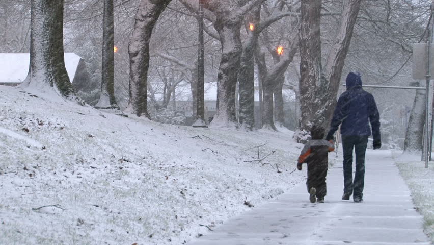 Young child and mother bundled up in winter gear, walk in snow storm in