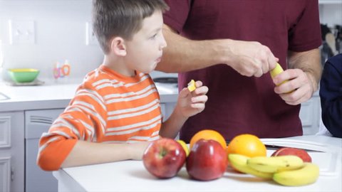 A father cuts up fruit for his three young children to eat.