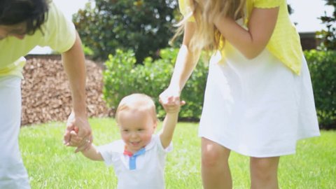Parents Helping Little Boy Practice Walking Barefoot Park - Healthy happy young male Caucasian child practicing walking grass outdoors park holding parents hands