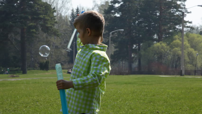 Cute little boy is making big bubbles in the park
