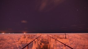 Night frozen sea ise coast and old iron pier - on moving ships and stars skyes timelapse
