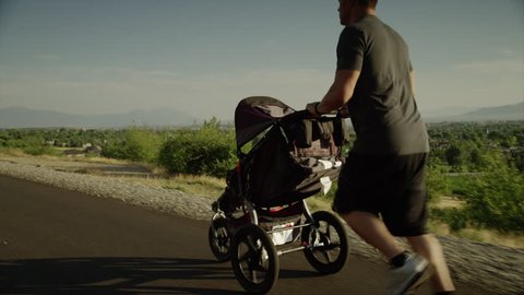 Tracking medium shot of man with baby carriage running on road 