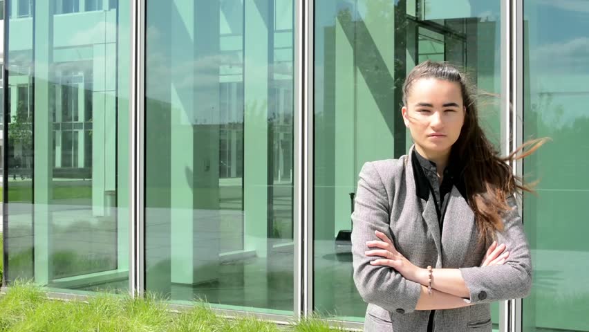 Business women has serious expression and stands before business building 