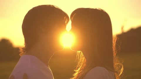 Romantic young couple silhouette is kissing on a sunset with sun shining bright behind them on a horizon. Slow motion filmed at 250 fps. First kiss of young love. 