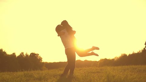 Romantic young couple silhouette. Woman is running to her man, they hug and spin around on a sunset with sun shining bright behind them on a horizon. Slow motion filmed at 250 fps. 