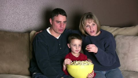 Family watching a suspenseful movie while eating popcorn